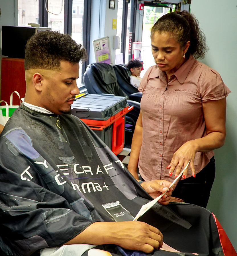 Clara Diaz speaks with Bladimir Taveras (in chair), owner of Gold Star Barbershop, 488 Hartford Ave., Providence., on July 6, 2022.