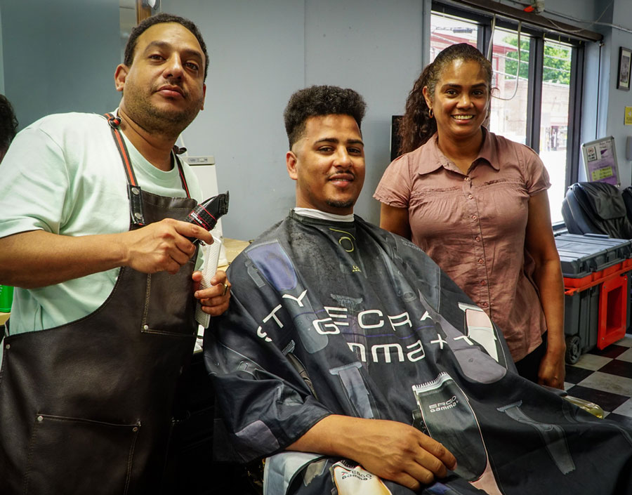 Clara Diaz poses with with barber Chanell Infonte, left, and Bladimir Taveras (in chair), owner of Gold Star Barbershop, 488 Hartford Ave. Diaz delivered information about the Central Providence Community Loan Fund.