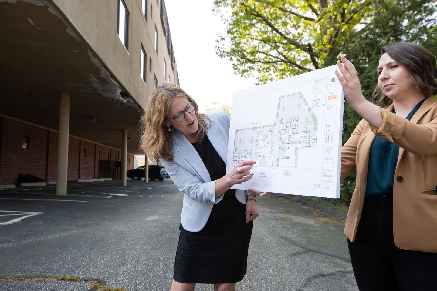 Jennifer Hawkins, president and executive director of One Neighborhood Builders (left) points to a mock up held by Grace Evans of One Neighborhood that features their project at 350 Taunton Avenue in East Providence. MATTHEW HEALEY FOR THE BOSTON GLOBE